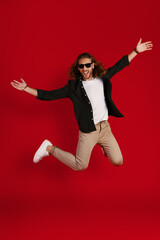 Full length of happy young man in casual clothing smiling and keeping arms outstretched while hovering against red background