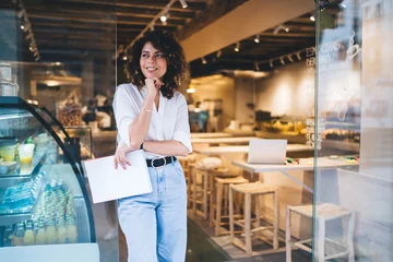 Foto op Plexiglas Happy female manager with menu in hand standing in doorway of local cafeteria and smiling, pretty Caucaisan small owner enjoying business lifestyle for working with franchise takeaway industry © BullRun