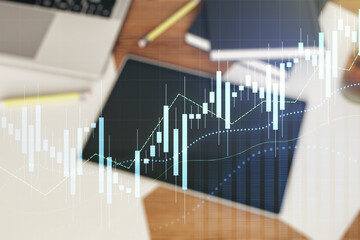 Multi exposure of abstract financial graph and modern digital tablet on desktop on background, top view, financial and trading concept
