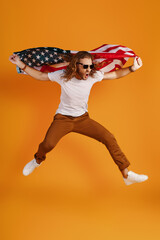 Fototapeta na wymiar Confident young man in casual clothing making a face and looking away while holding American flag against yellow background