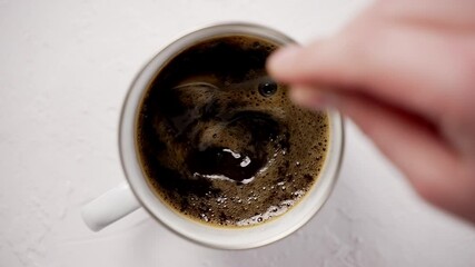 Hand stiring with a spoon a hot, black coffee in a metal mug