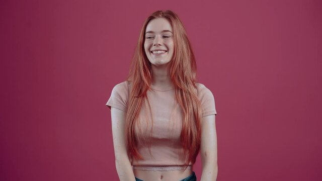 The victorious 20-year-old redhead, in a pink casual T-shirt, isolated on a pink background. The concept of people's lifestyle. Shocata points to the right and celebrates the victory with a wide smile
