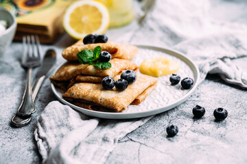 Crepes with homemade cottage cheese, blueberries and lemon curd on a gray plate