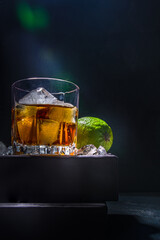 Whiskey or cognac in glass, with lime, ice cubes ans barmen utensils, dark background with on stand pedestal copy space