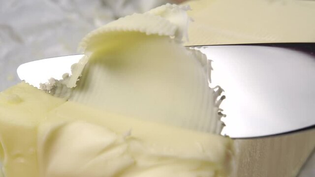 A kitchen knife cuts a piece of butter with a curl close-up. Beautiful fat thin shavings. Macro shot