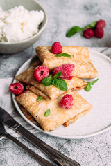 Crepes with homemade cottage cheese, raspberries a gray plate