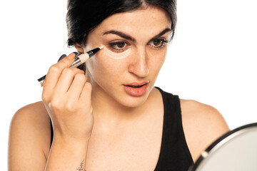 Obraz premium Half portrait of young beautiful woman applying concealer