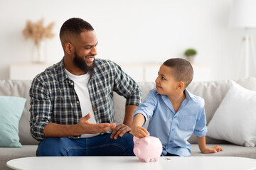 Father And Son Putting Personal Savings Money In Piggybank Indoor