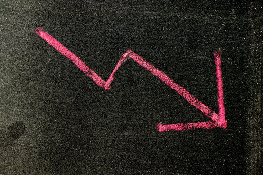 Red color chalk handdrawing in arrow down shape on blackboard or chalkboard background (Concept of stock decline, down trend of business, economy)