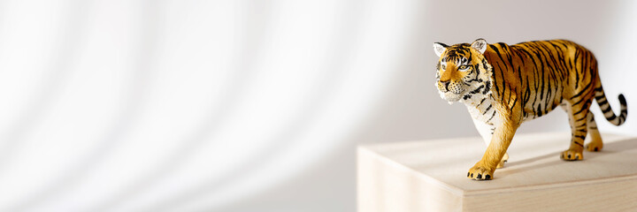 Tiger symbol of the Chinese new year 2022. Figurine of tiger on wooden stand on white background with shadows. Copy space. Banner