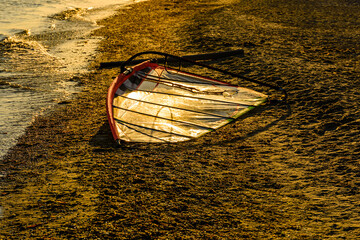 Windsurfing sail on a sand at the sea shore on sunset