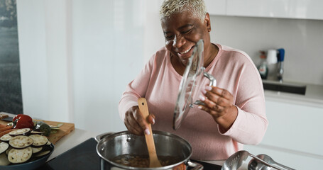 Happy black senior woman cooking healthy food inside kitchen