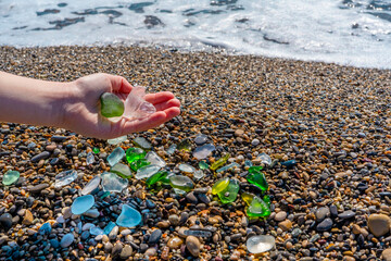 Colorful polished pieces of sea glass collected from the beach in a child hand. Beautiful close-up sea green, blue and white glass on a sea beach background.
