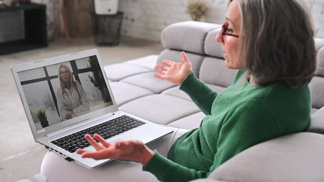 Middle aged woman making video call with a female doctor, talking about healthy, complains disease symptoms, staying at home at quarantine. Telemedicine concept