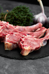 Raw lamb chops with garlic, herbs on black ceramic plate over white stone gray table. Top view. With copy space