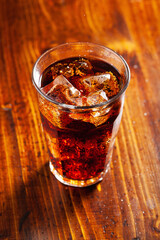glass of cold cola soft drink with ice on wooden background