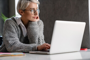 White-haired focused woman working with laptop while sitting at table