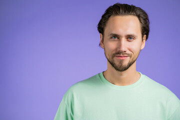 Fototapeta premium Portrait of cheerful european man looking to camera. Copy space. Young handsome kind guy smiling in studio on violet background.