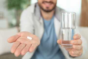 young man showing pill and glass of water