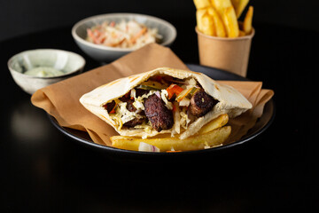 Beef pita with vegetables on black plate, food close up