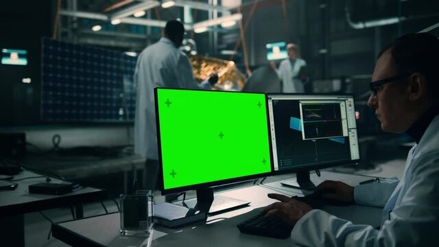 Male Engineer Uses Green Screen Mock Up Display Computer to Analyse Satellite. Aerospace Agency Manufacturing Facility: Scientists Develop, Assemble Spacecraft for Space Exploration Mission.