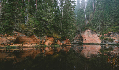 Sandstone cliffs and a beautiful evergreen forest by the Brasla river in Latvia during cloudy day