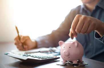 Close-up image of man hand putting coins in pink piggy bank for account save money. Planning step...