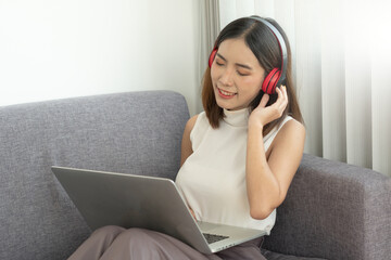 A young Asian woman is happily relaxing listening to music through wireless headphones while at home on vacation.