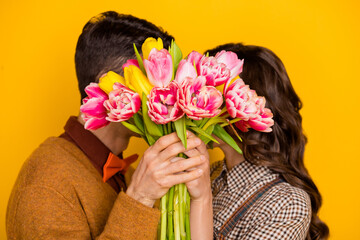 Photo of charming man and woman hold hands flowers cover close face kiss isolated on yellow color background