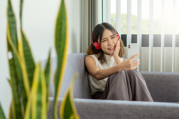 A young Asian woman wears headphones wirelessly, connects to a bluetooth system with a mobile...