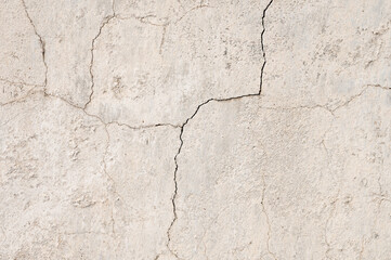 Grunge background of cracked peeling walls with peeled putty in beige tones.