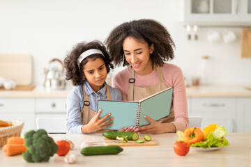 Black woman and girl cooking in kitchen reading recipe book