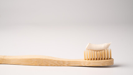 Eco dental concept. Natural toothpaste on a bamboo toothbrush. Wooden toothbrush on white...