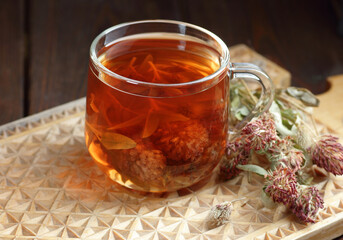 Red clover tea in glass cup on wood on rustic background of wicker, herbal drink is good for menopause, bone, heart health and for skin and hair care, closeup, naturopathy and natural medicine concept