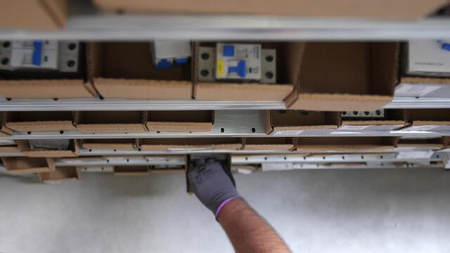 Worker with gloves takes an electrical component from a shelf