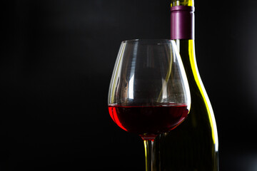Wine bottle and glass with red wine on dark glossy background.