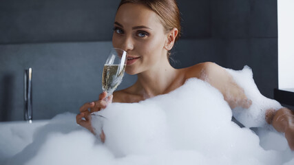 young woman taking bath with foam and drinking champagne in white bathtub © LIGHTFIELD STUDIOS