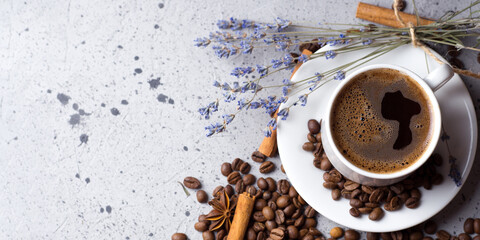 A cup of aromatic espresso coffee on a white table, a stick of cinnamon, anise, scattered roasted coffee beans, copy space banner