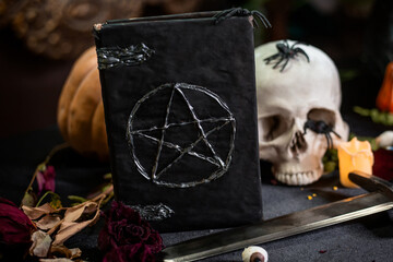 Focus on a black book with a pentagram lying on a black table against a background of a skull and...