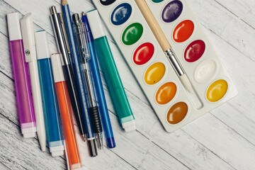 Naklejka premium watercolor paints colored pencils and markers on wooden table top view
