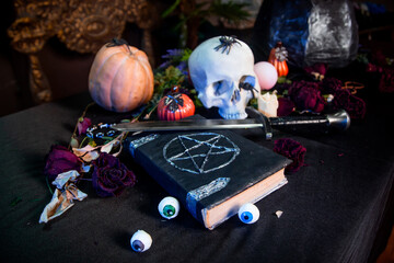Focus on a black book with a pentagram lying on a black table against a background of a skull and...
