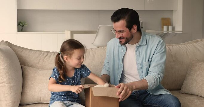 Preschool girl sit on couch with loving dad, family open received parcel enjoy surprise, take out fluffy toy bear and gift box. Quick express delivery, e-commerce online services happy clients concept
