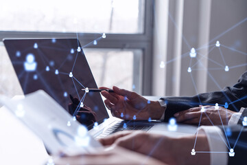 Two HR specialists analyzing the recruitment market using laptop to boost the intern program at international consulting company. Social networking hologram icons.