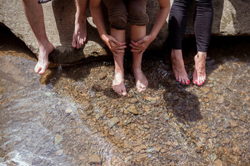 Friends feet playing and having fun time on the mountain creek. Siblings sitting on the rock at waterfall, feet in the water of a river full of stones. Barefoot people washing feet in river.