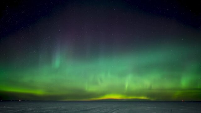 Dramatic Northern Lights, Aurora, above a frozen snow covered lake with a few lights from distant homes along the horizon
