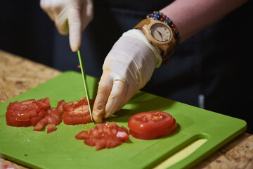 Slicing tomatoes with a knife on a board with gloves