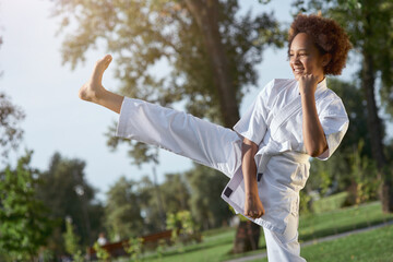 Joyful little girl in kimono practicing karate on the street
