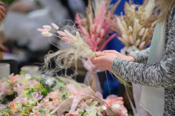 business owner selling behind counter with her bouquet of dried flowers at local market of craftsmen, small business. young woman entrepreneur sells floral holiday composition.
