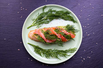 delicious slices of crispy baguette with avocado and smoked salmon fillet and fresh dill sprigs on a green plate