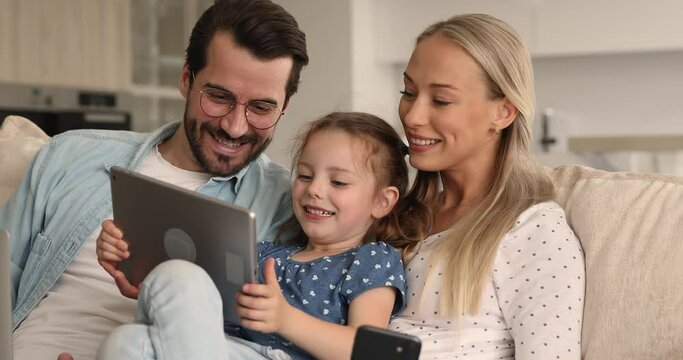 Little girl spend time with parents hold diverse devices, child use tablet having fun on internet, enjoy new app for children, watch cartoons, family addicted with gadgets, modern tech overuse concept